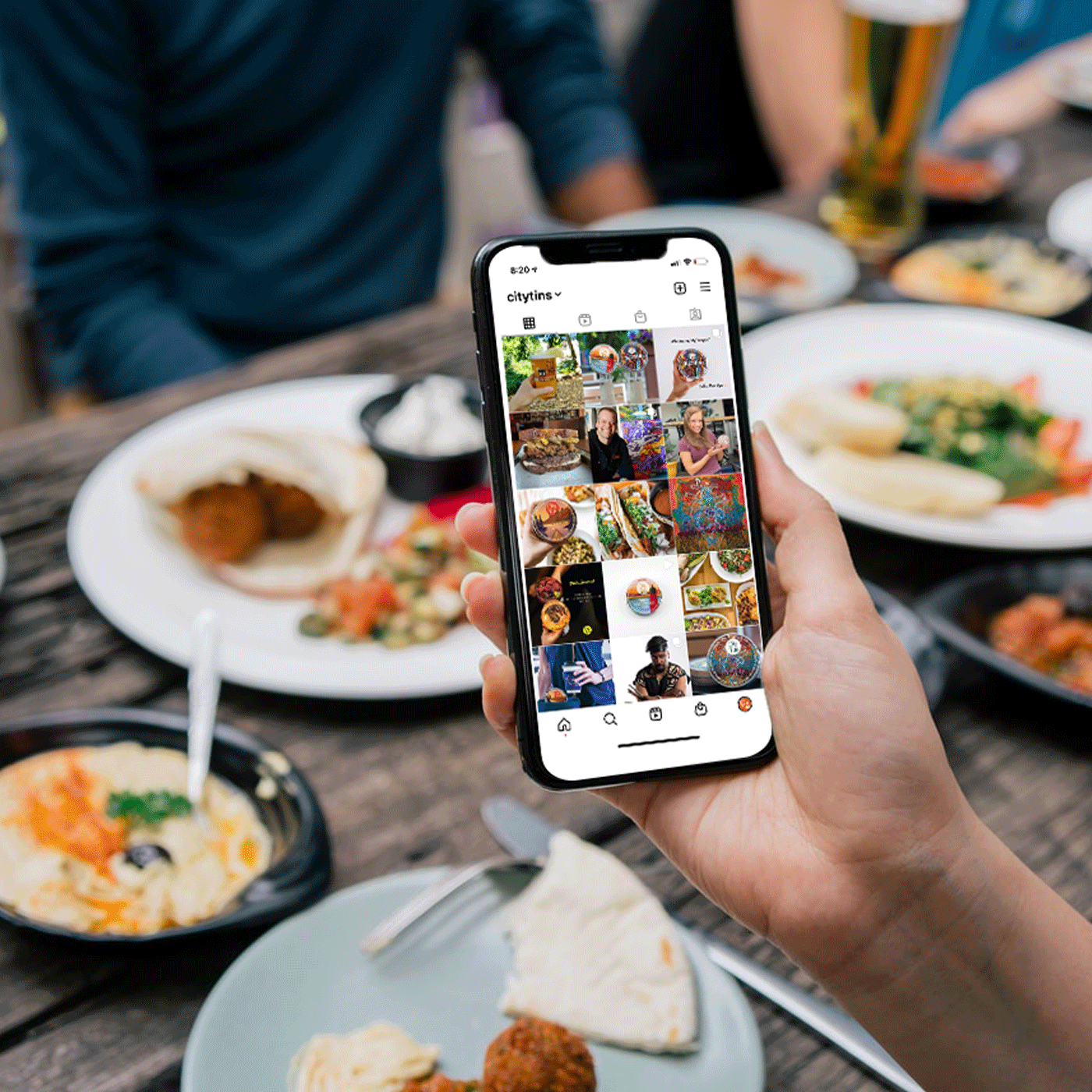 Woman holding phone as she views CityTins Instagram amidst an outdoor farm-to-table dining experience.